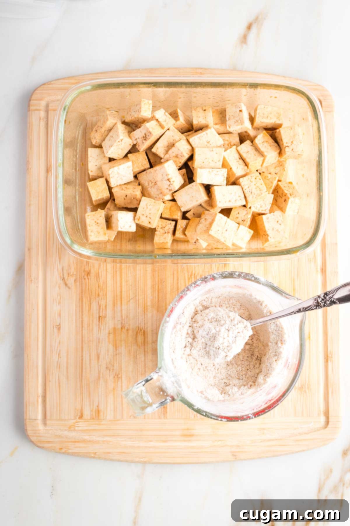 Cup of spiced arrowroot powder next to a dish of tofu cubes.