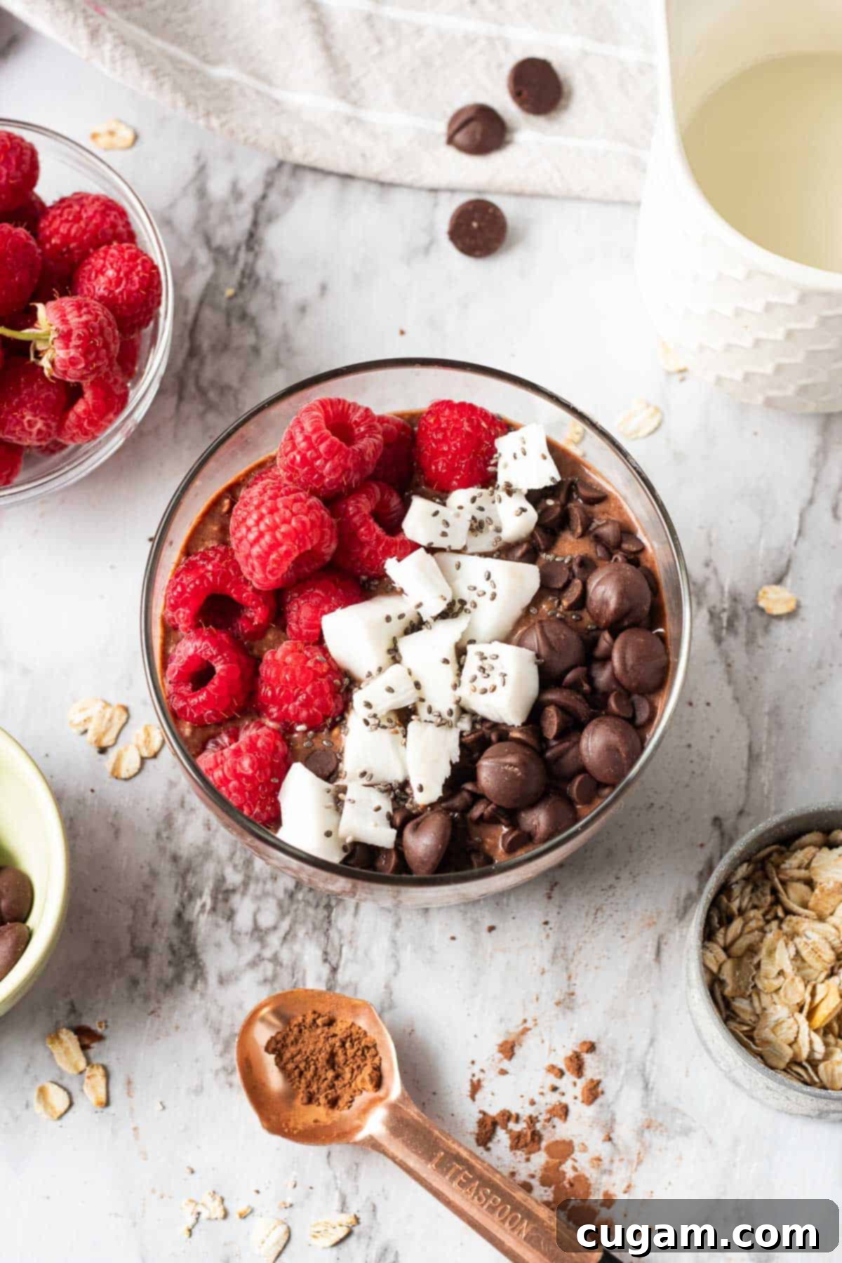 Brownie Batter Overnight Oats with spoonful of cocoa powder and bowl of raspberries nearby.