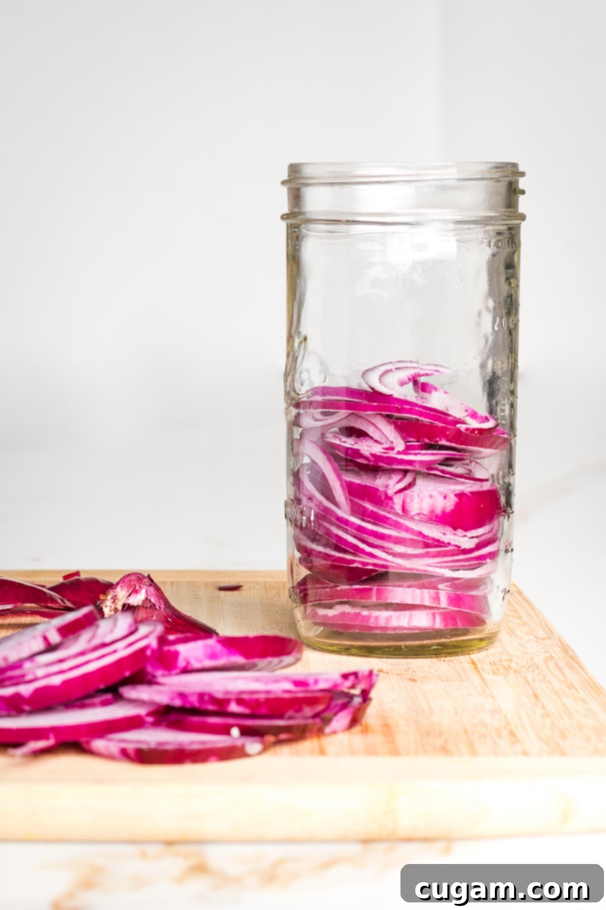 Slices of red onion on a cutting board and loaded into a mason jar.