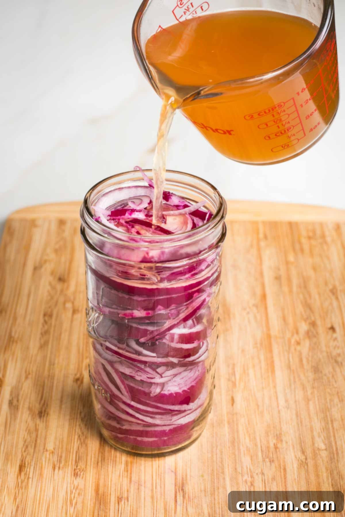 Pouring brownish liquid over slices of red onions in a jar.