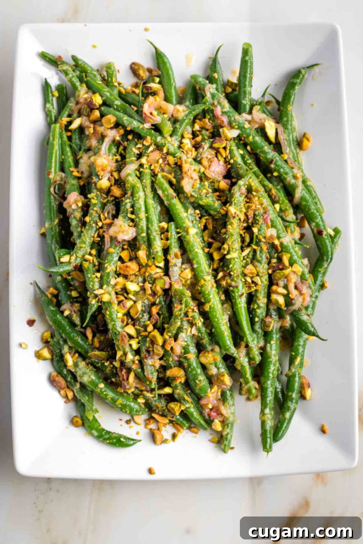 Green beans on a platter with dressing and pistachios.