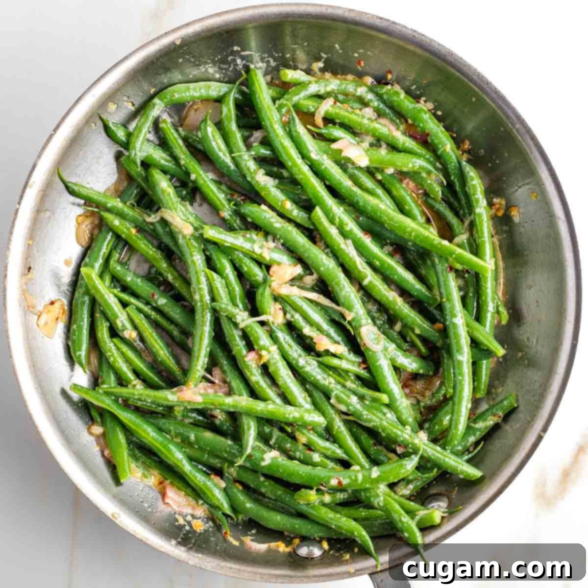 Skillet filled with saucy green beans including some fried lemony shallots. 
