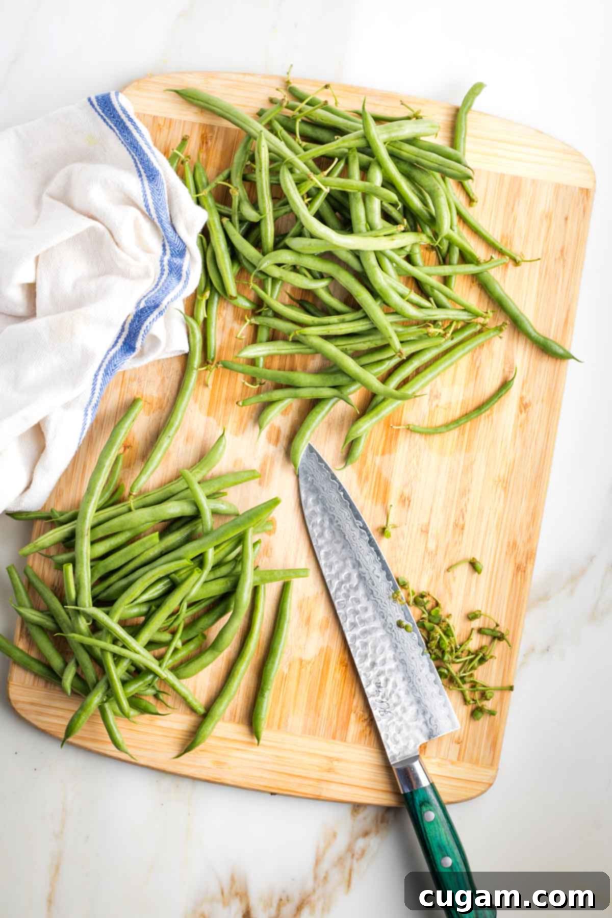 Cutting the stem side off a pile of green beans on a cutting board.