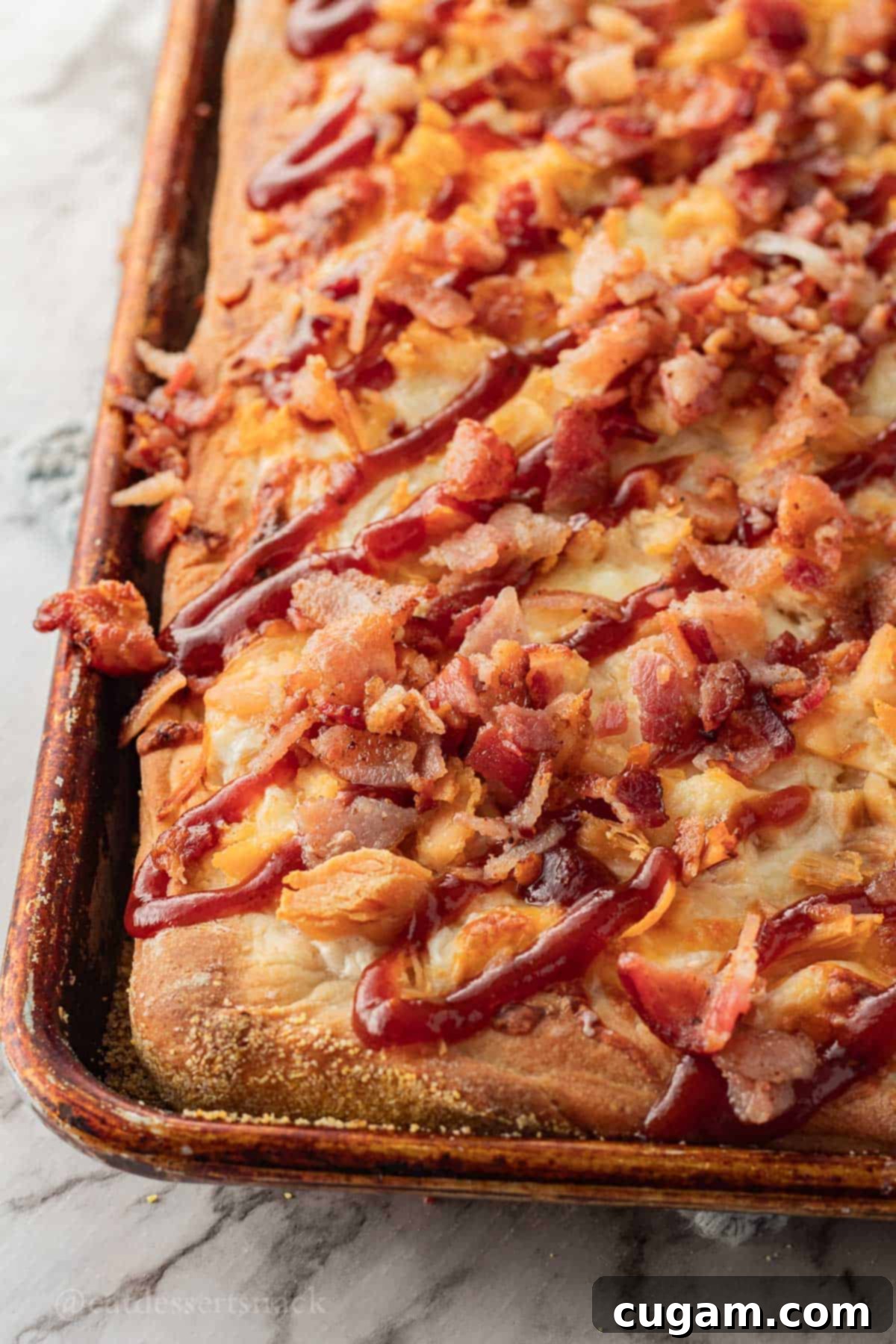 Baked BBQ chicken bacon ranch pizza in a metal sheet pan, sitting on a beautiful marble countertop, ready to be sliced and served.