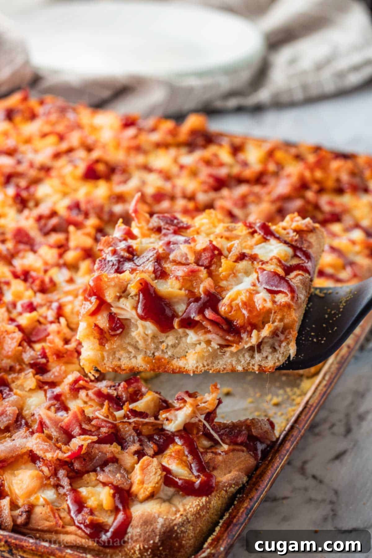 A perfect slice of BBQ bacon chicken ranch pizza held on a black spatula, showing its crispy crust and abundant toppings.