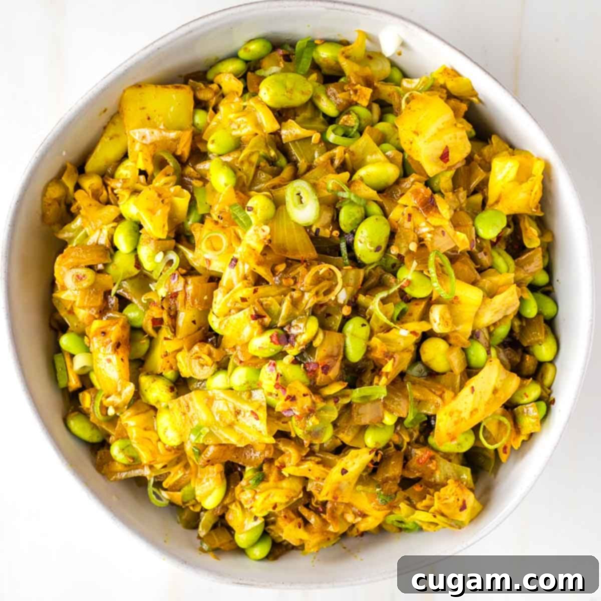 Cooked cabbage chunks with edamame, scallions and crushed red pepper in a serving bowl.