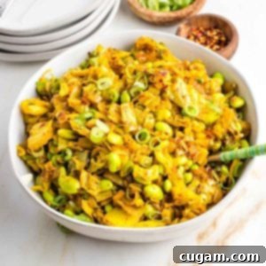 Bowl full of chopped cabbage with onions and edamame in a yellow curry, garnished with sliced scallions.