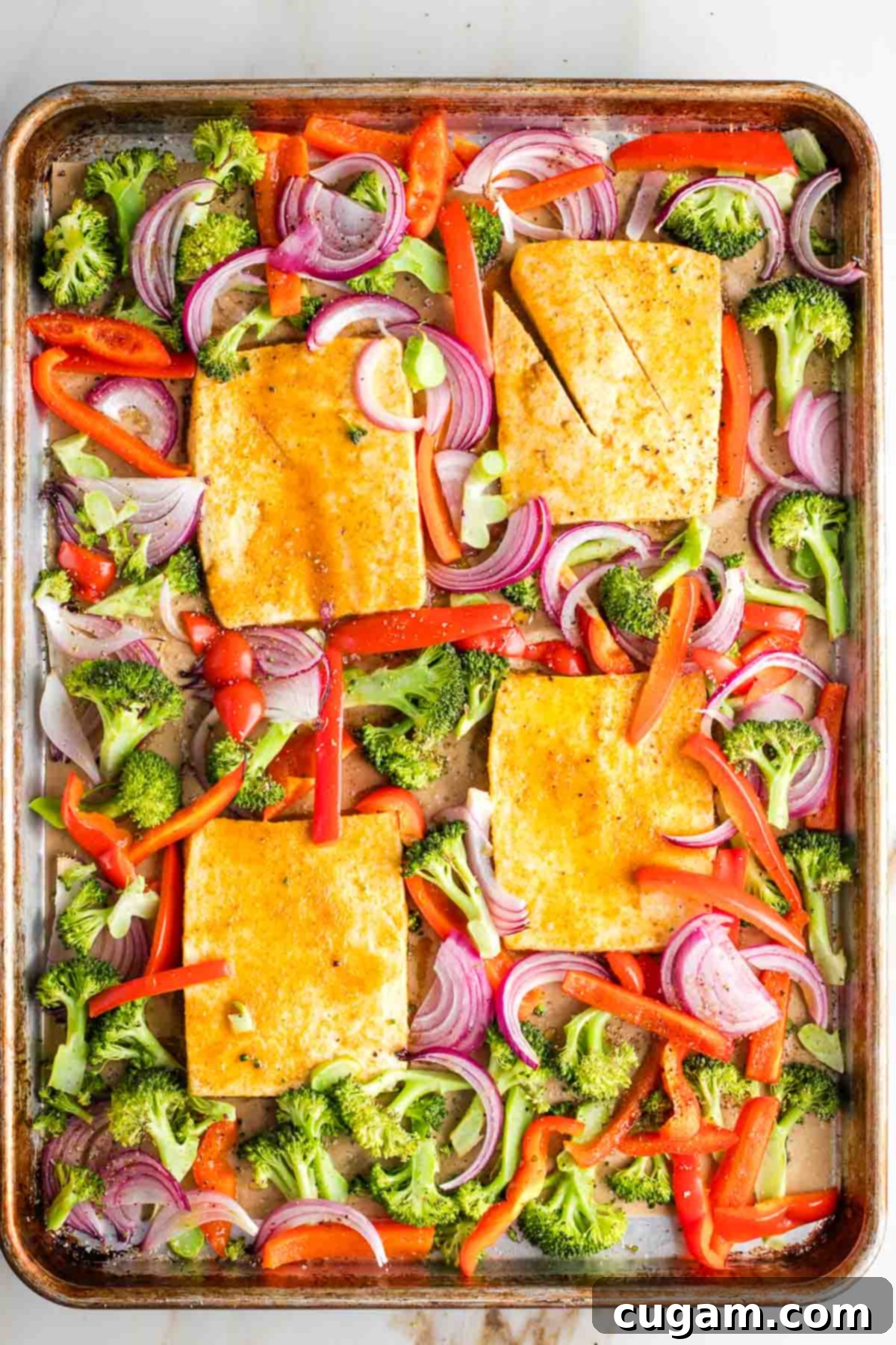 Large baking tray with slabs of tofu surrounded by broccoli, red peppers and onions.