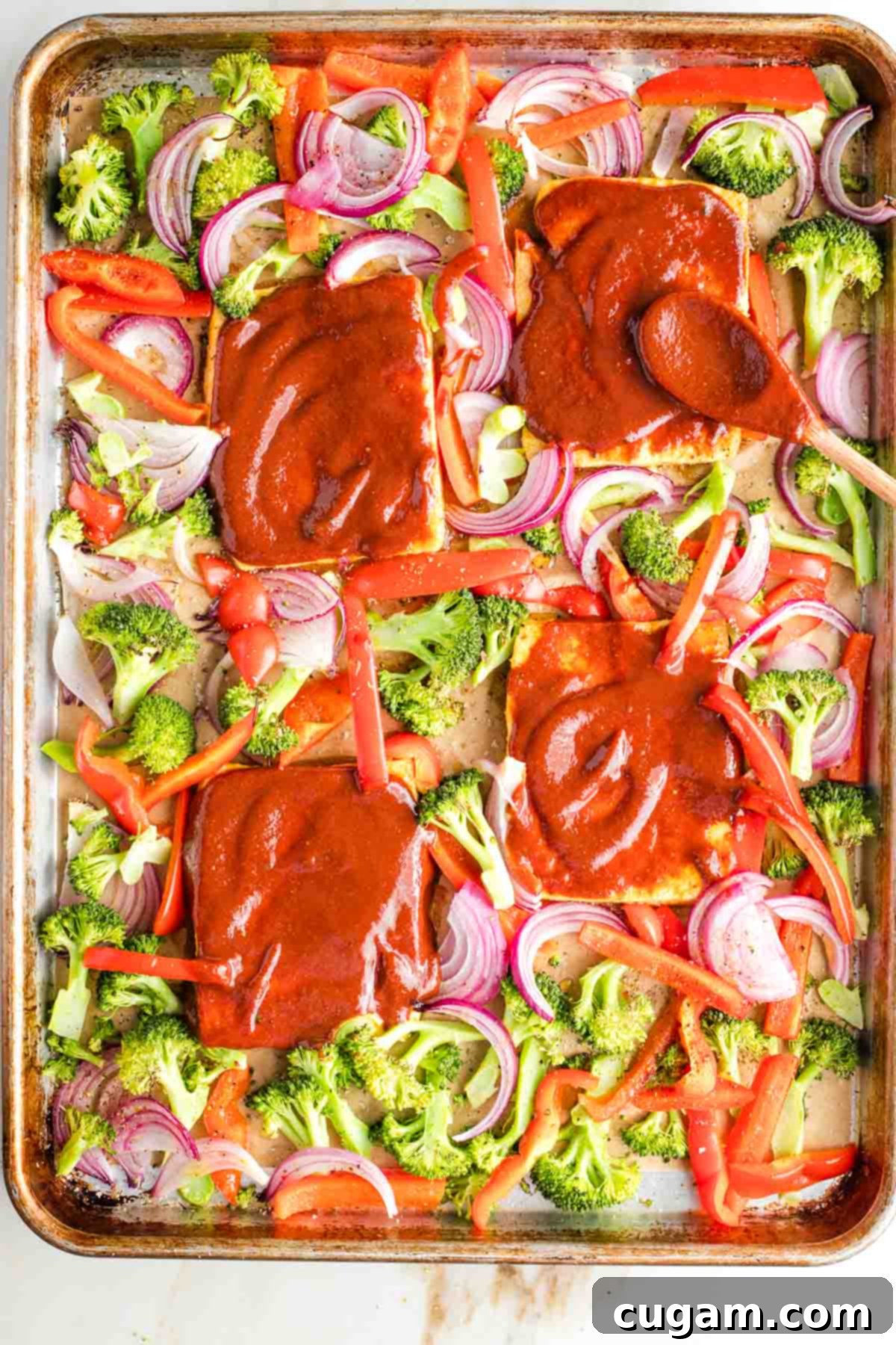 Tofu steaks smothered in bbq sauce on a sheet pan with broccoli, red peppers and onions sprinkled around.