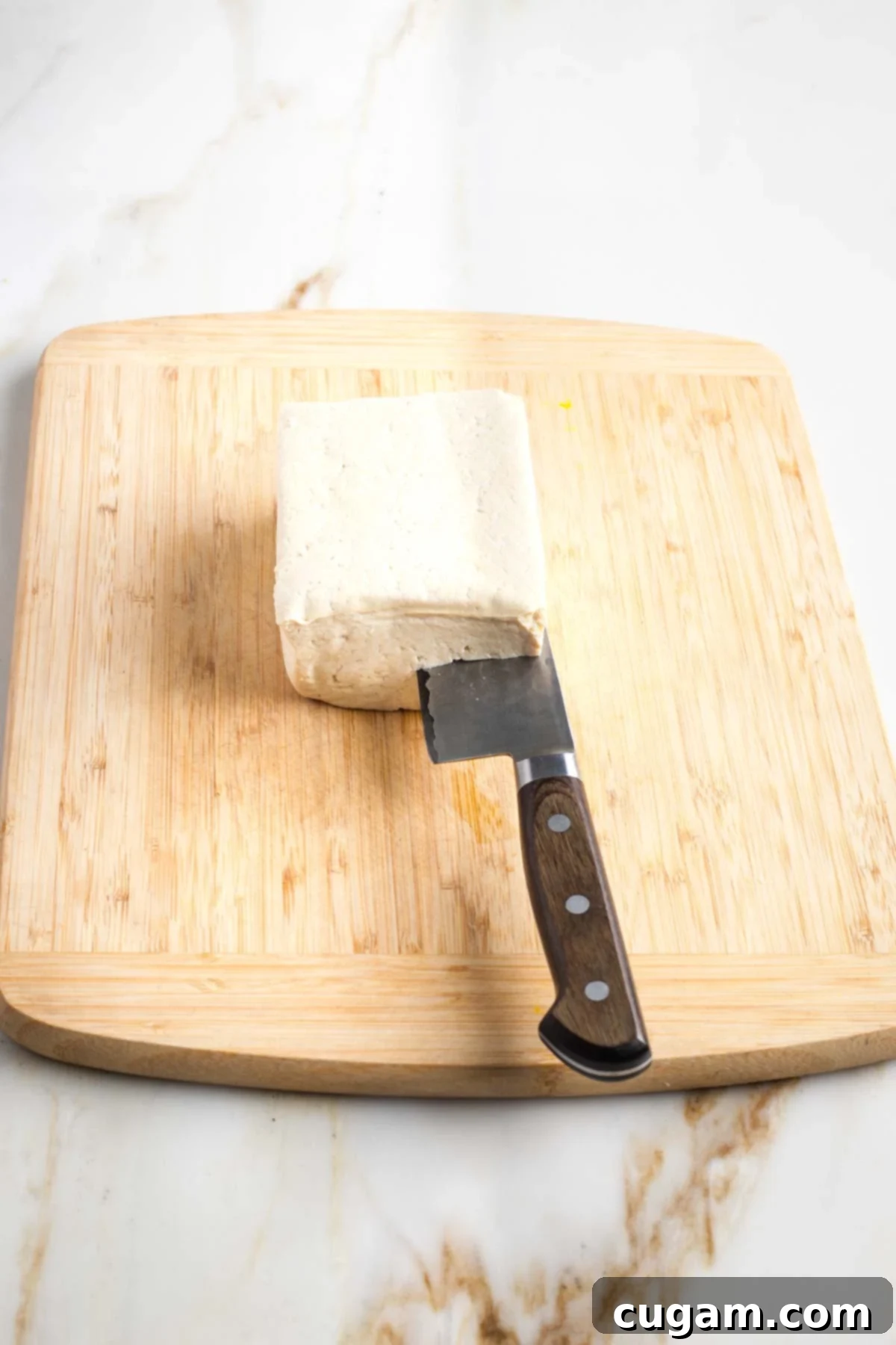 Knife cutting through crosswise a block of tofu to create two slabs.