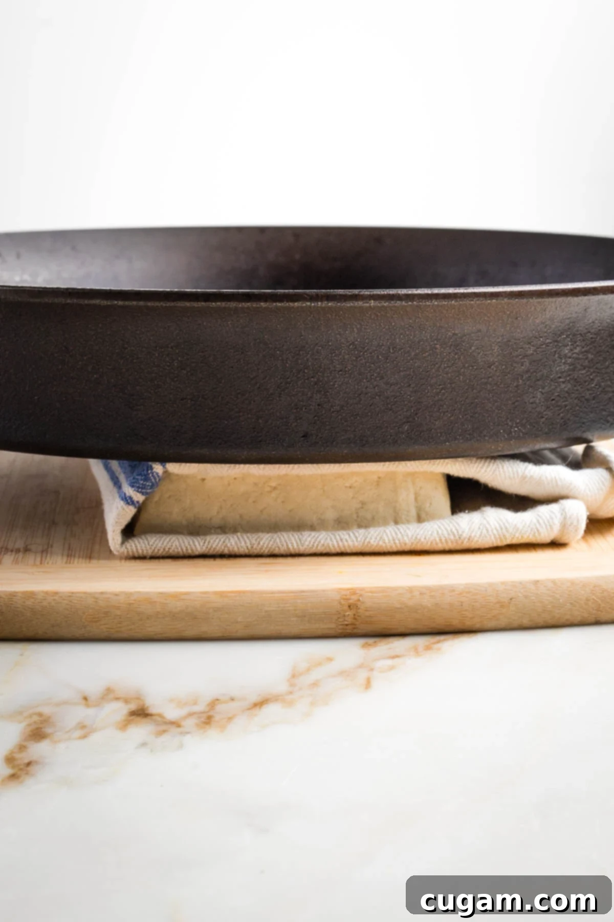 Cast iron pan on top of a block of tofu wrapped in a kitchen towel.