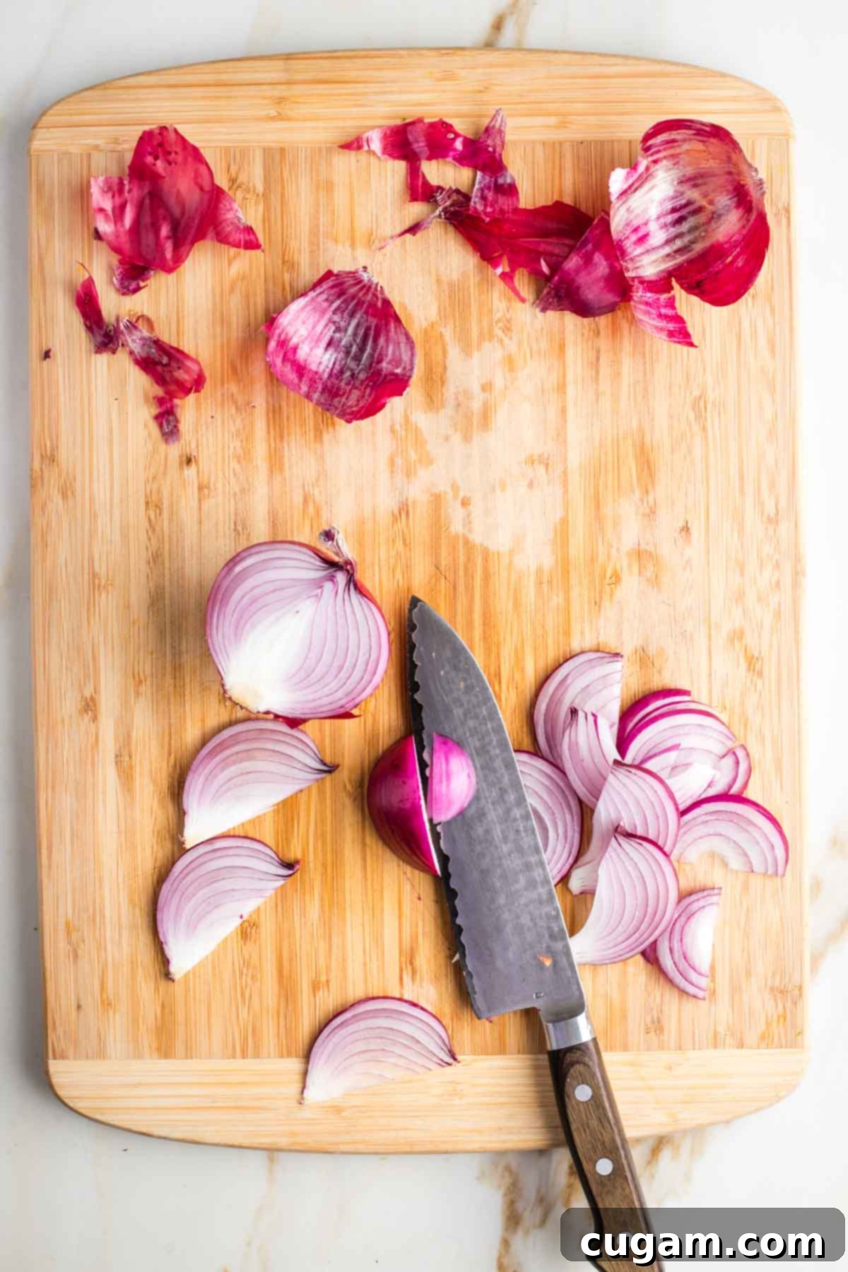 Red onion, cut in half and then into thin slices.Onion skins are still on the cutting board.