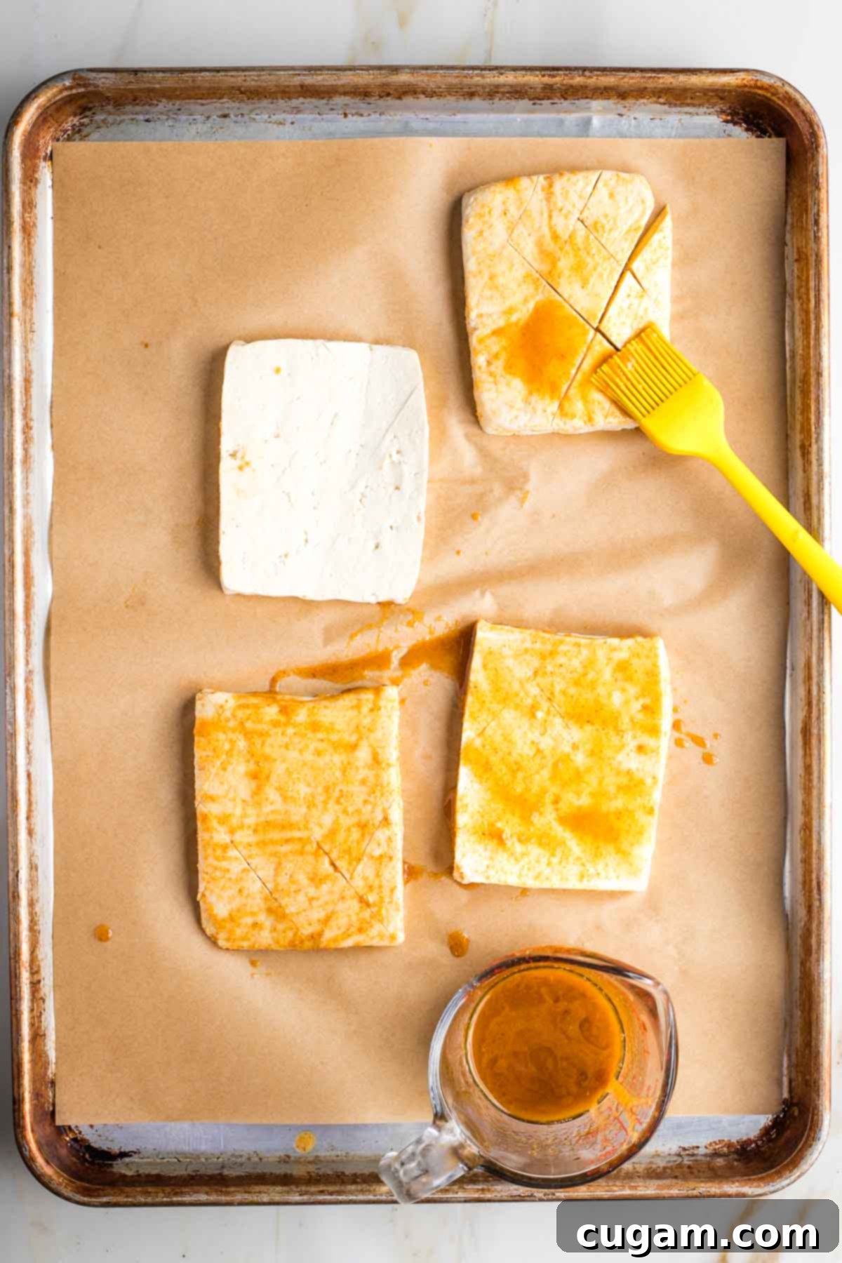 Basting tofu steaks with marinade on a large rimmed baking sheet.