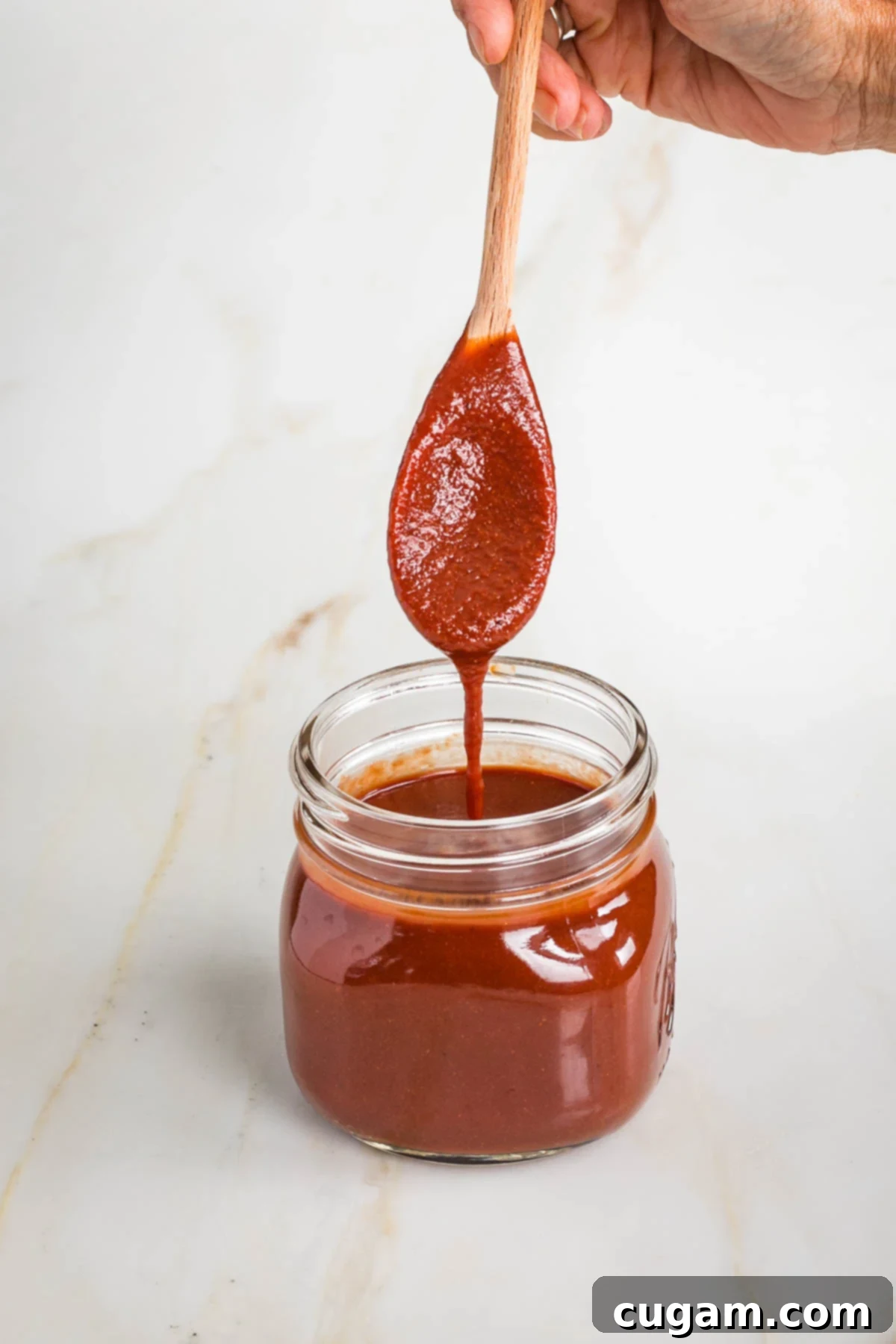 Spoon popping out of a jar of bbq sauce, thickly coated and dripping.