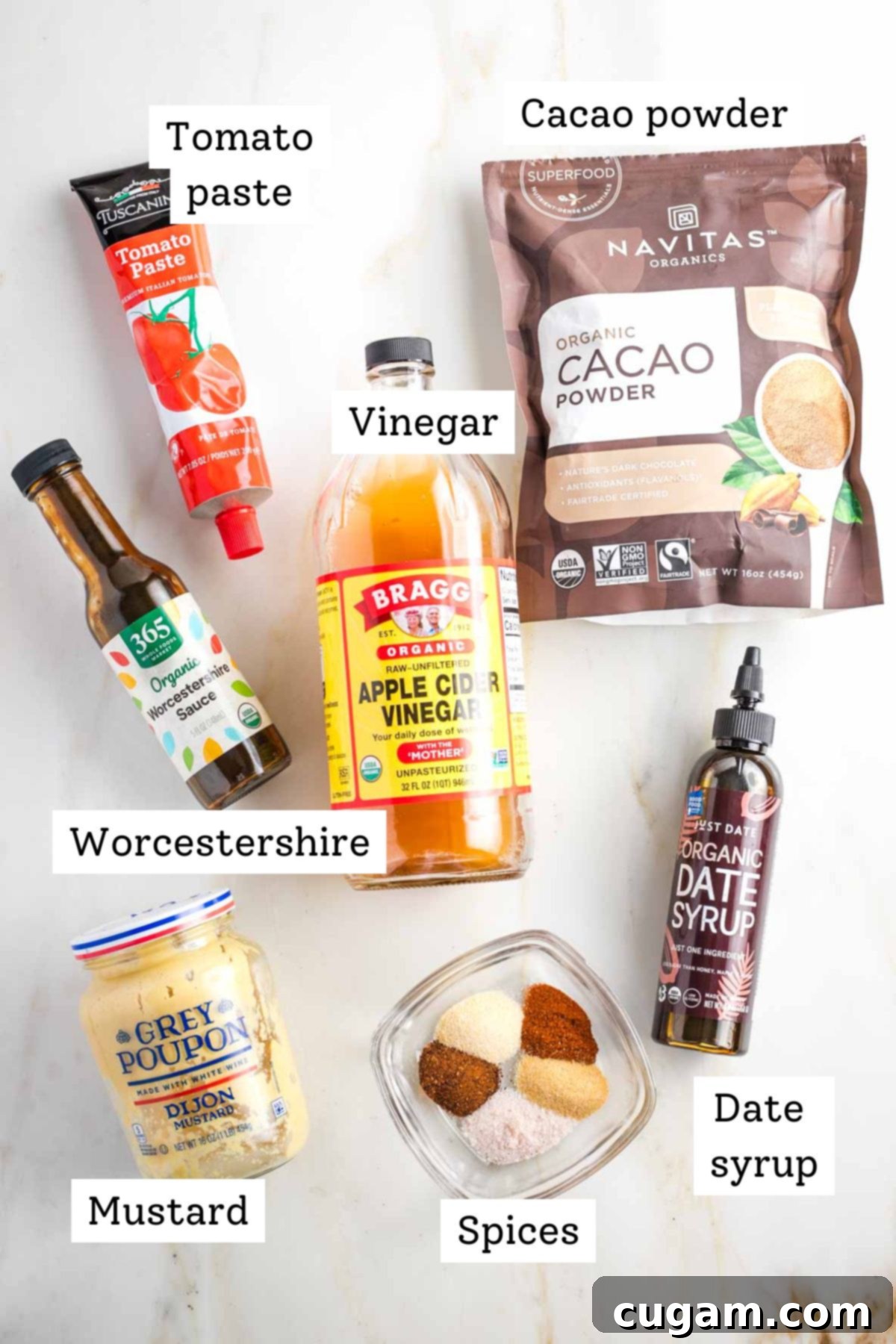 A beautifully arranged flat lay of essential ingredients for the no-cook BBQ sauce: vibrant tomato paste, earthy cacao powder, tangy apple cider vinegar, natural date syrup, spicy dijon mustard, savory Worcestershire sauce, and aromatic spices.