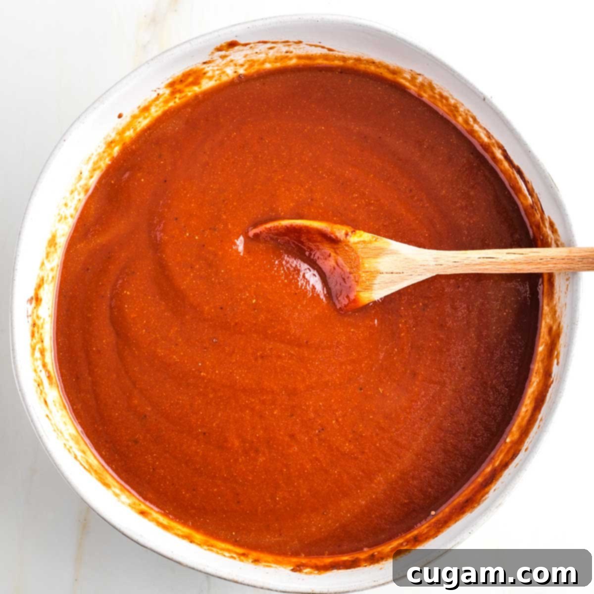 Stirring bbq sauce in a white bowl with wooden spoon.