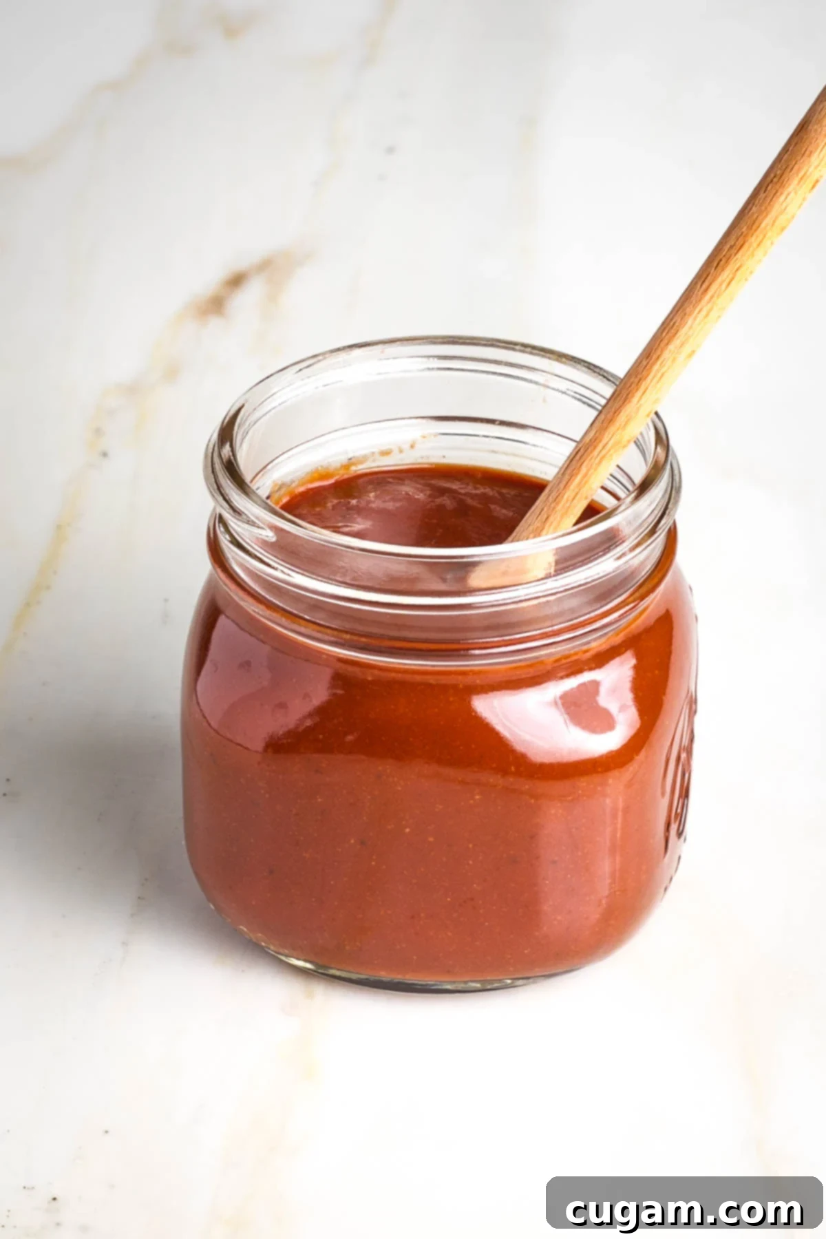 Jar of bbq sauce with wooden spoon sticking out of the top.