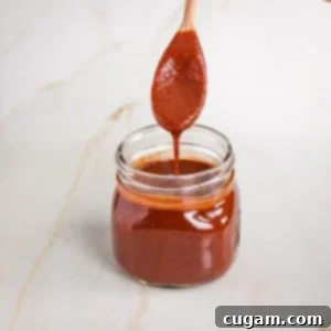 Spoon of deep red colored bbq sauce pulling out of a jar.