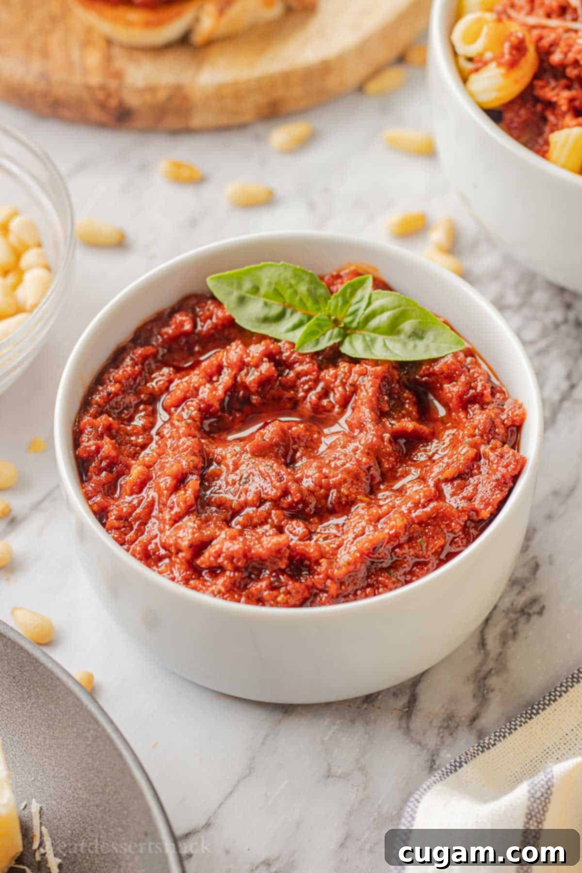 Blended red pesto in white bowl on marble countertop.