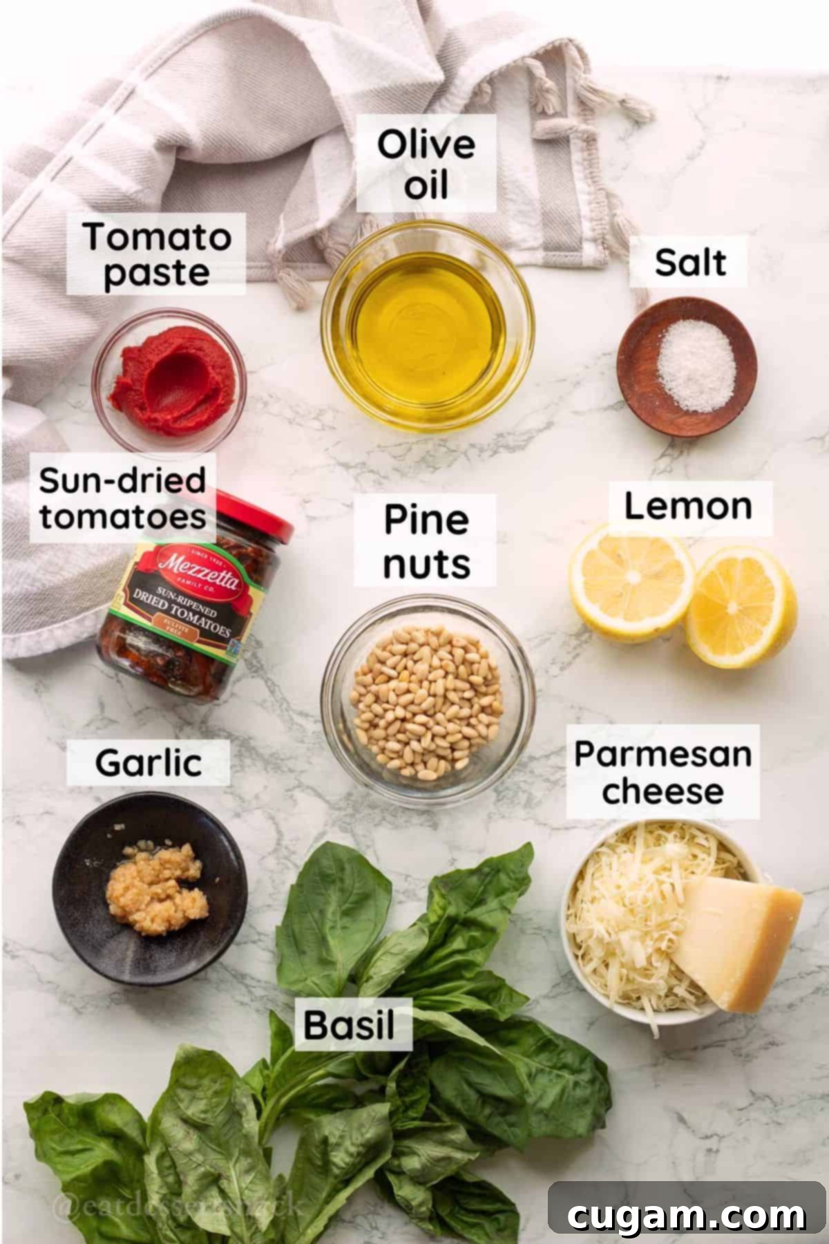 Labeled ingredients for red pesto sauce in glass bowls on marble countertop.