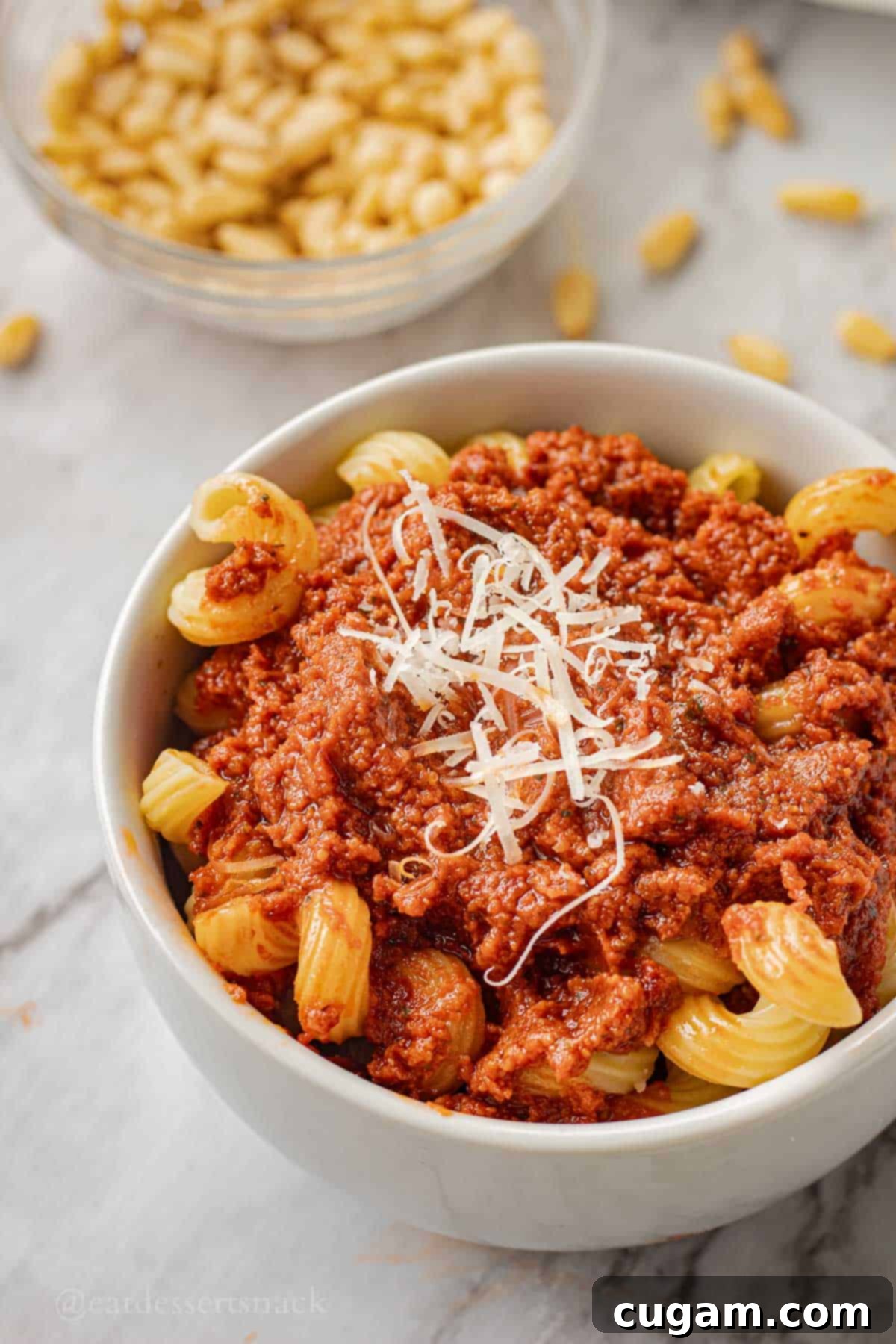 Red pesto sauce with parmesan cheese on pasta in white bowl.