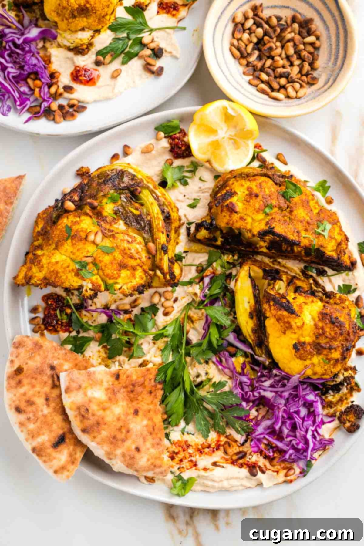 Platter of roasted cauliflower shawarma on top of hummus with toasted pine nuts, fresh parsley, cabbage and lemon.