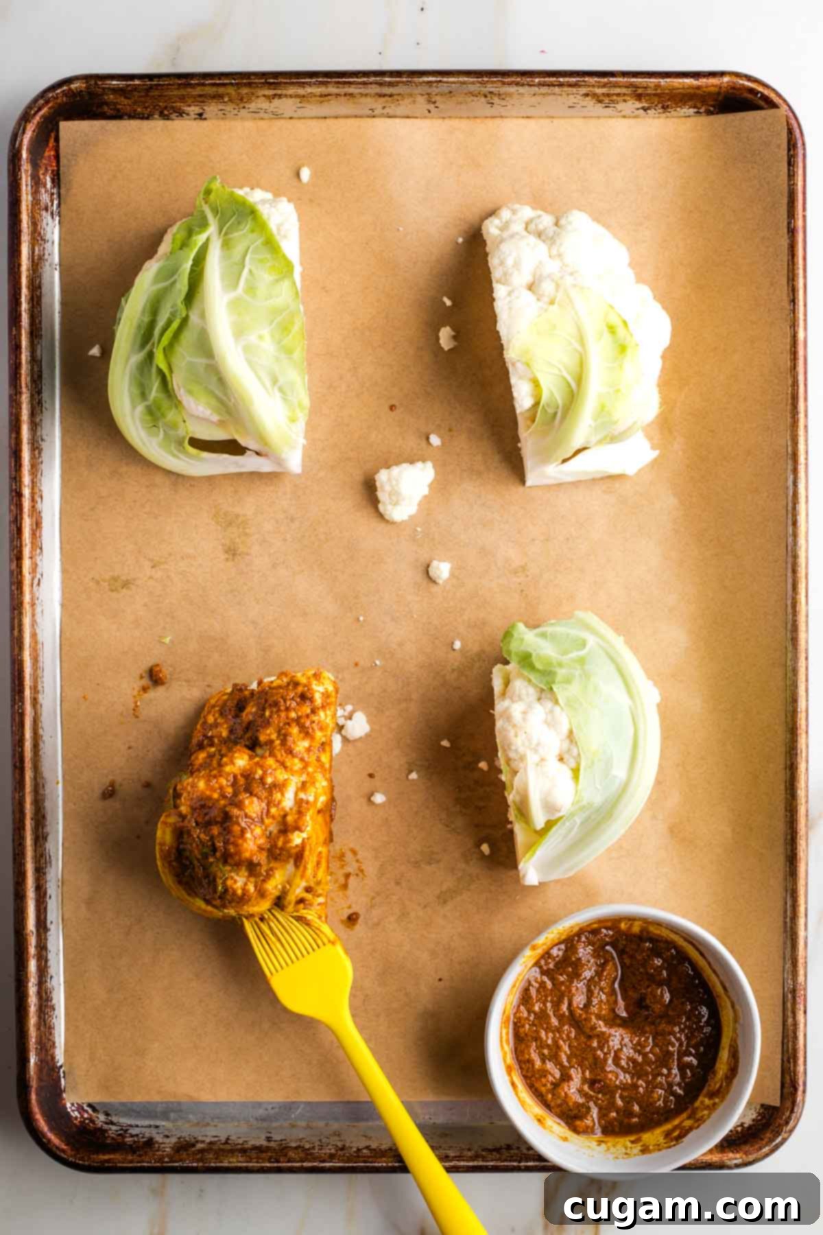 Brushing shawarma paste onto cauliflower ¼s on a rimmed baking sheet.