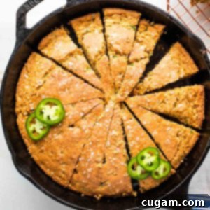 Corn bread with jalapenos cut into pie slices inside a cast iron skillet.