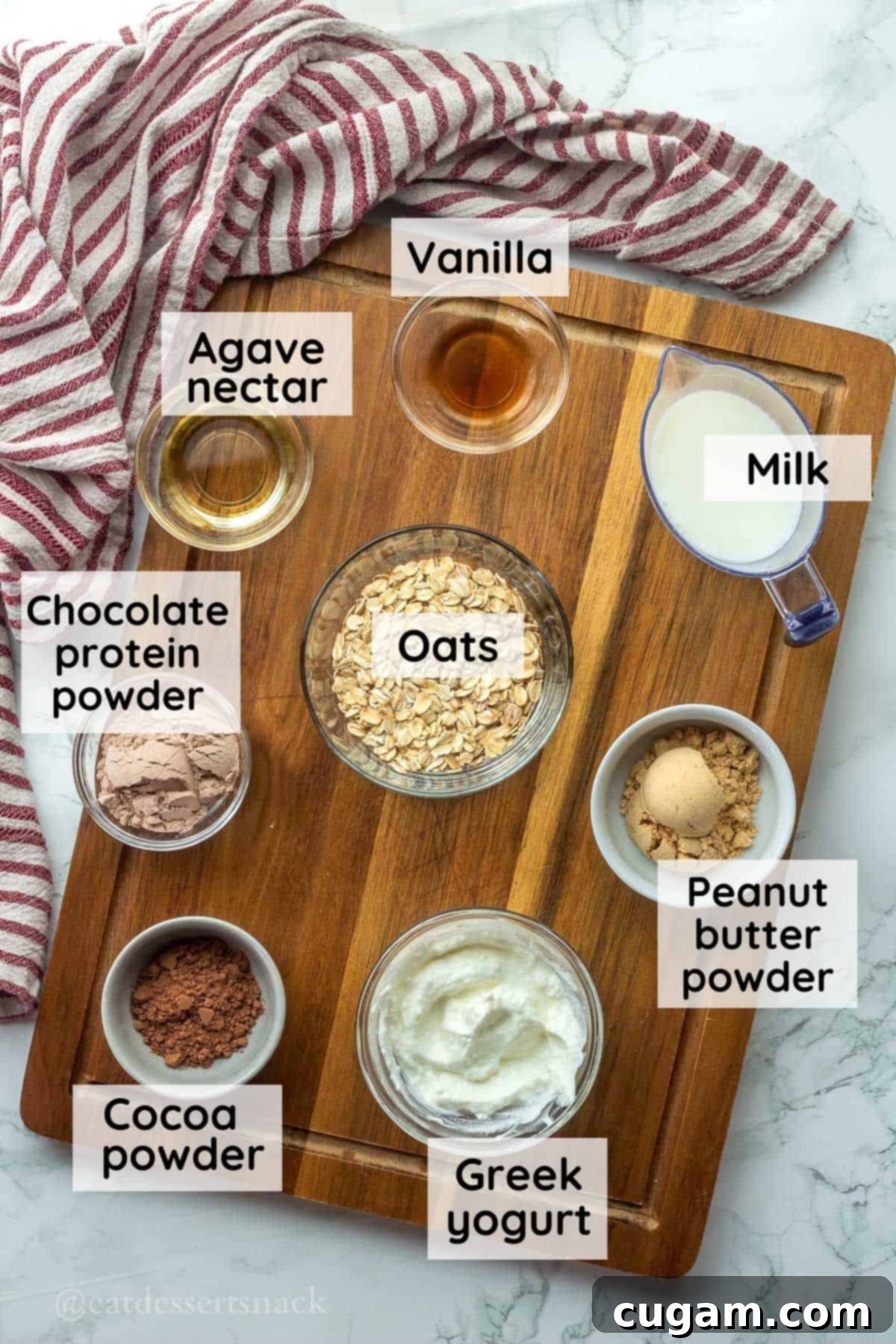 Selection of key ingredients for Chocolate Peanut Butter Protein Overnight Oats laid out on a wooden cutting board: rolled oats, milk, plain Greek yogurt, vanilla extract, chocolate protein powder, cocoa powder, and peanut butter powder in individual glass bowls.
