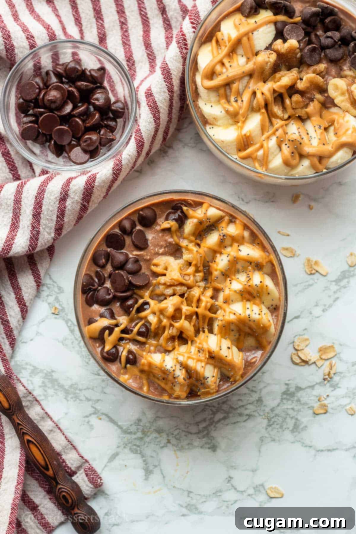 Two glass bowls of prepared chocolate peanut butter overnight oats sit on a marble countertop, ready for chilling, highlighting their rich color and smooth texture.