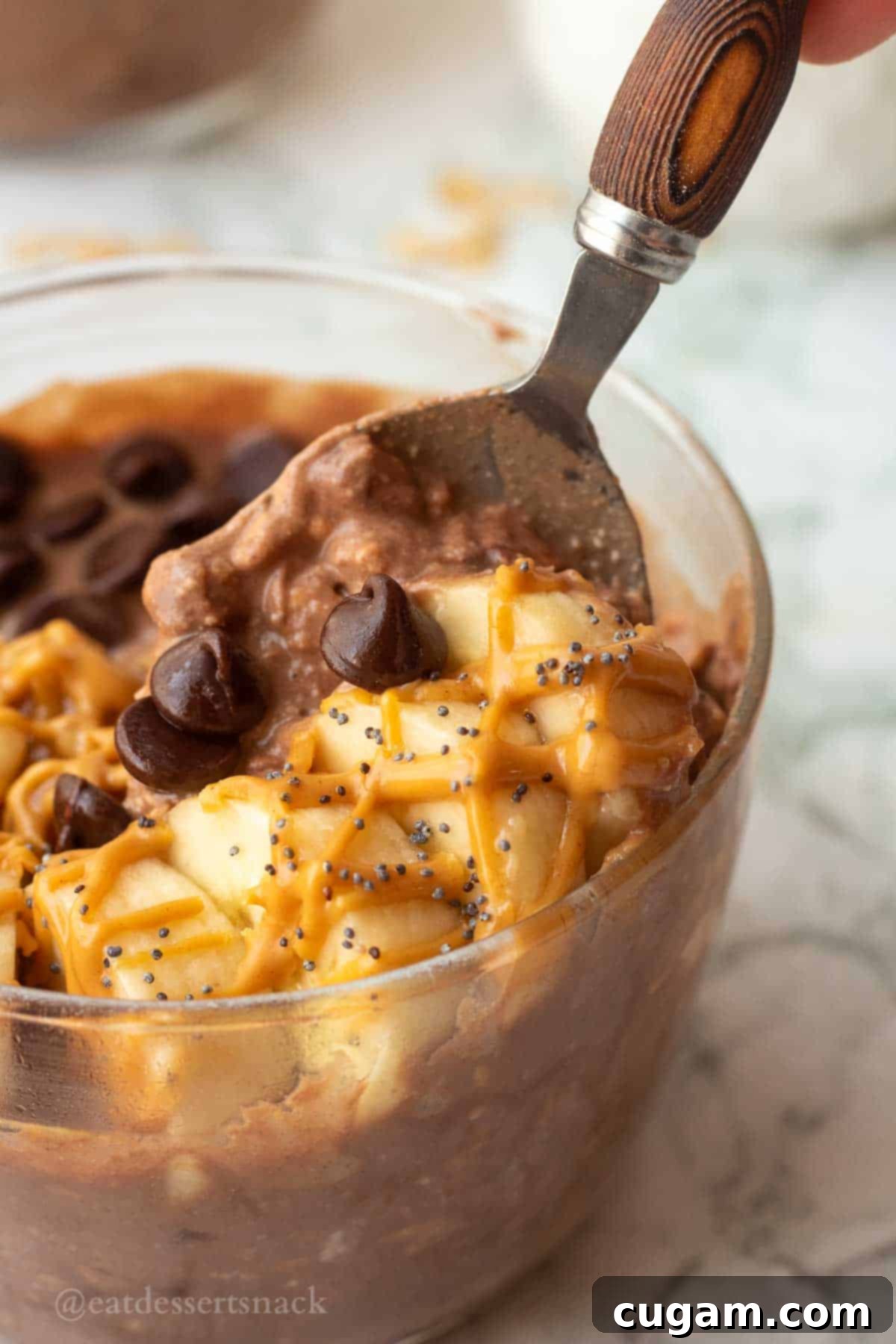 Wooden handled spoon holding up banana slices and chocolate peanut butter overnight oats, showcasing the layers of flavor and toppings.