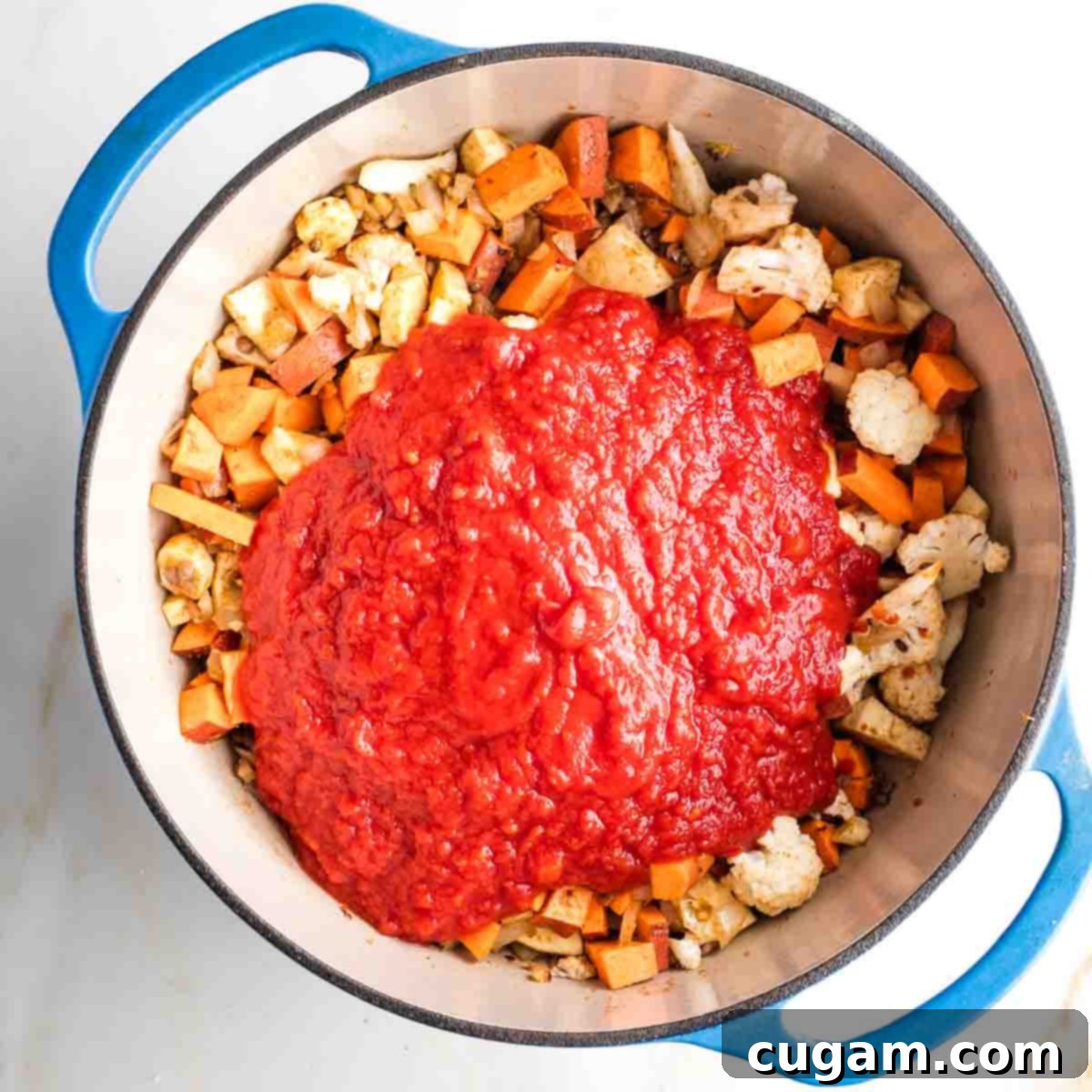 Crushed tomatoes on top of sauteed veggies in a dutch oven.