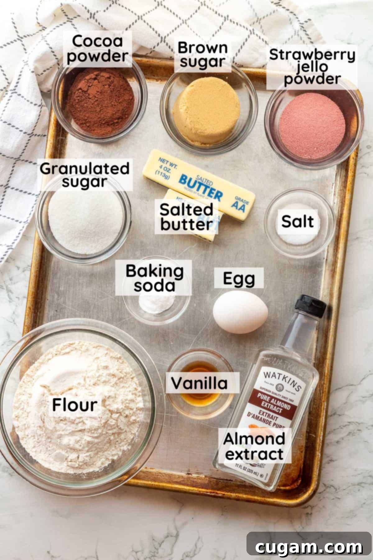 Neapolitan Layered Cookies 3 Array of labeled ingredients for Neapolitan cookies, including butter, sugars, cocoa, jello, and flour, arranged in glass bowls on a metal baking sheet.