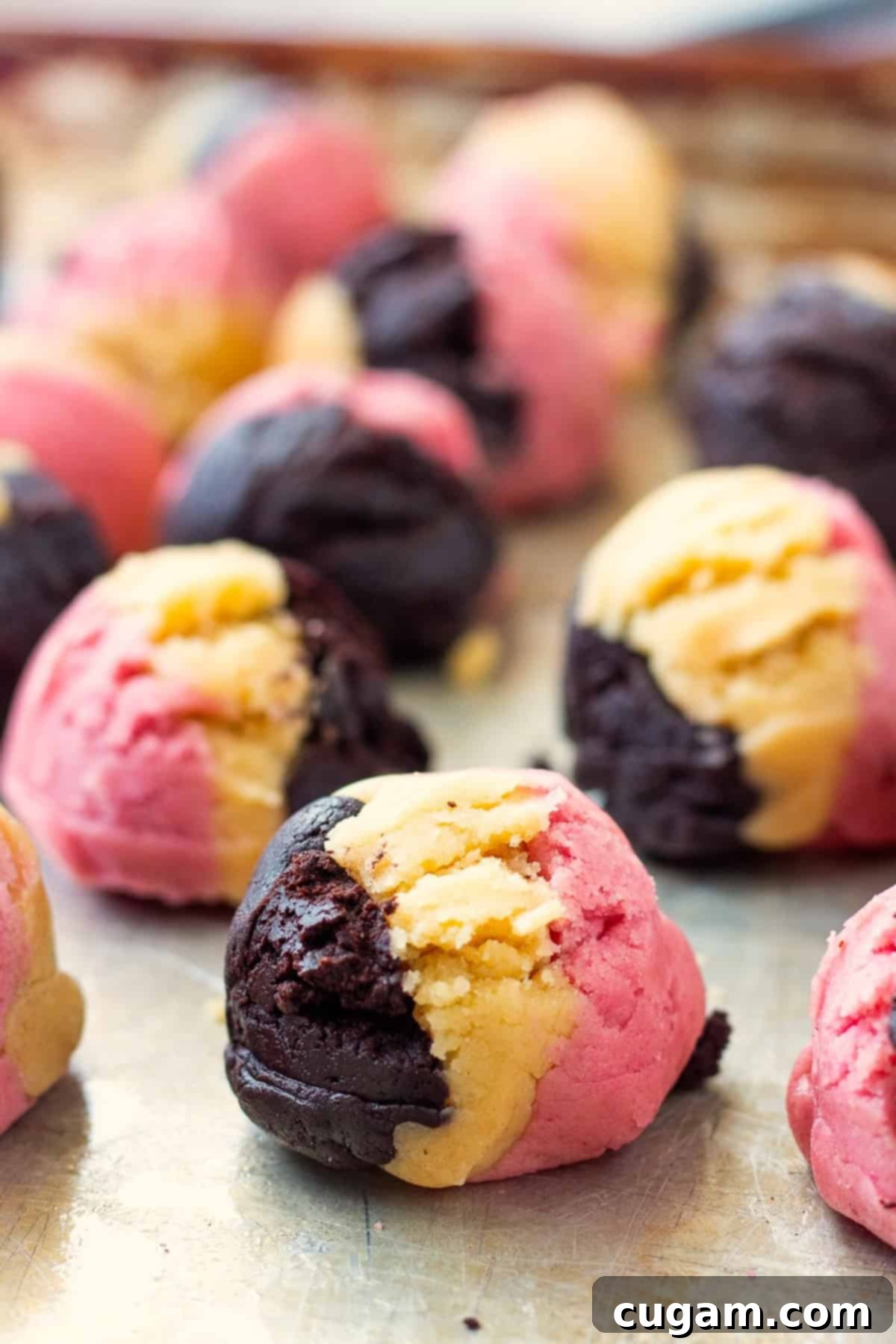 Neapolitan Layered Cookies 9 Raw Neapolitan cookie dough balls, clearly showing the distinct vanilla, chocolate, and strawberry colors, neatly arranged on a metal baking sheet, ready for baking.