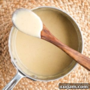 Bechamel sauce clinging to a wooden spoon resting atop a saucepan filled with the white sauce.