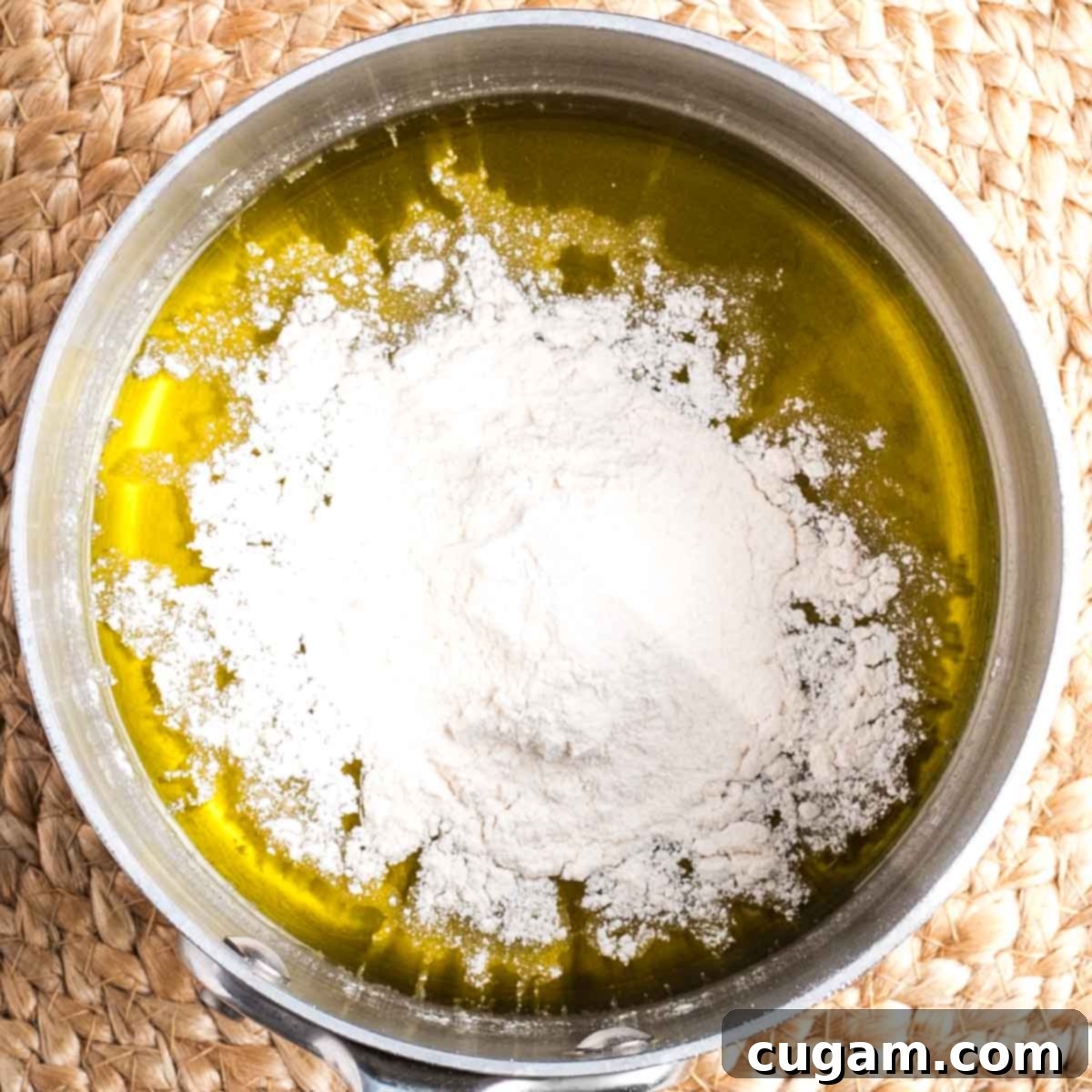 A small saucepan with olive oil at the bottom, lightly sprinkled with white cassava flour, ready to be whisked into a roux.
