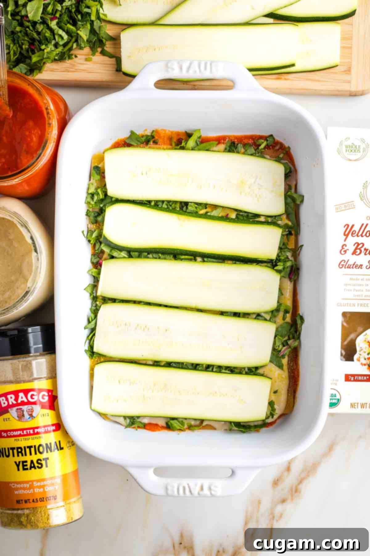 Thinly sliced zucchini topping layers of noodles and sauce in the making of a vegetable lasagna.