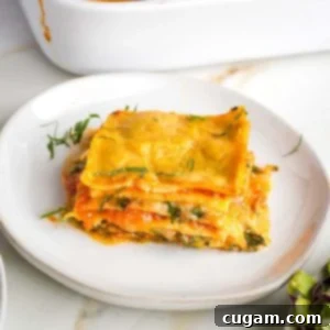Layers of noodles, greens, zucchini, bechamel and marinara shown on a side view of a piece of lasagna.