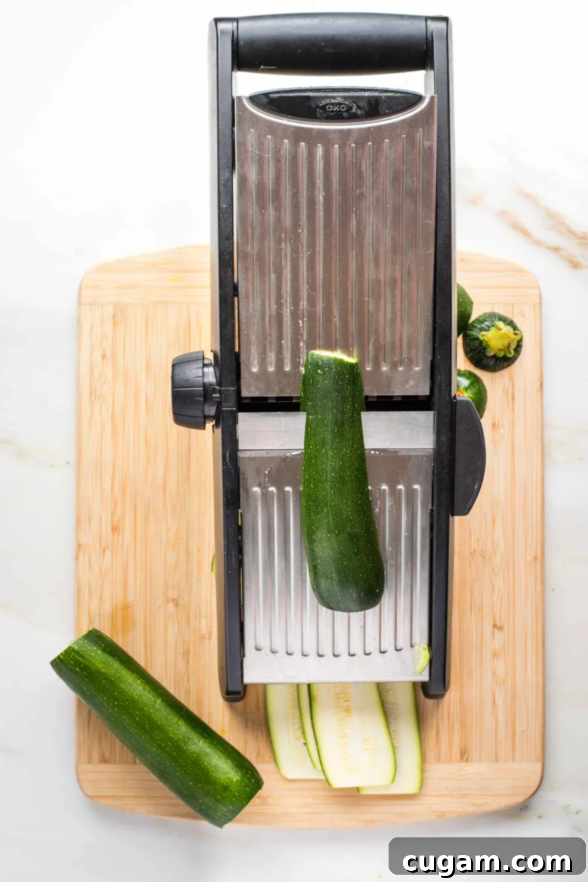 Mandolin thinly slicing zucchini lengthwise.
