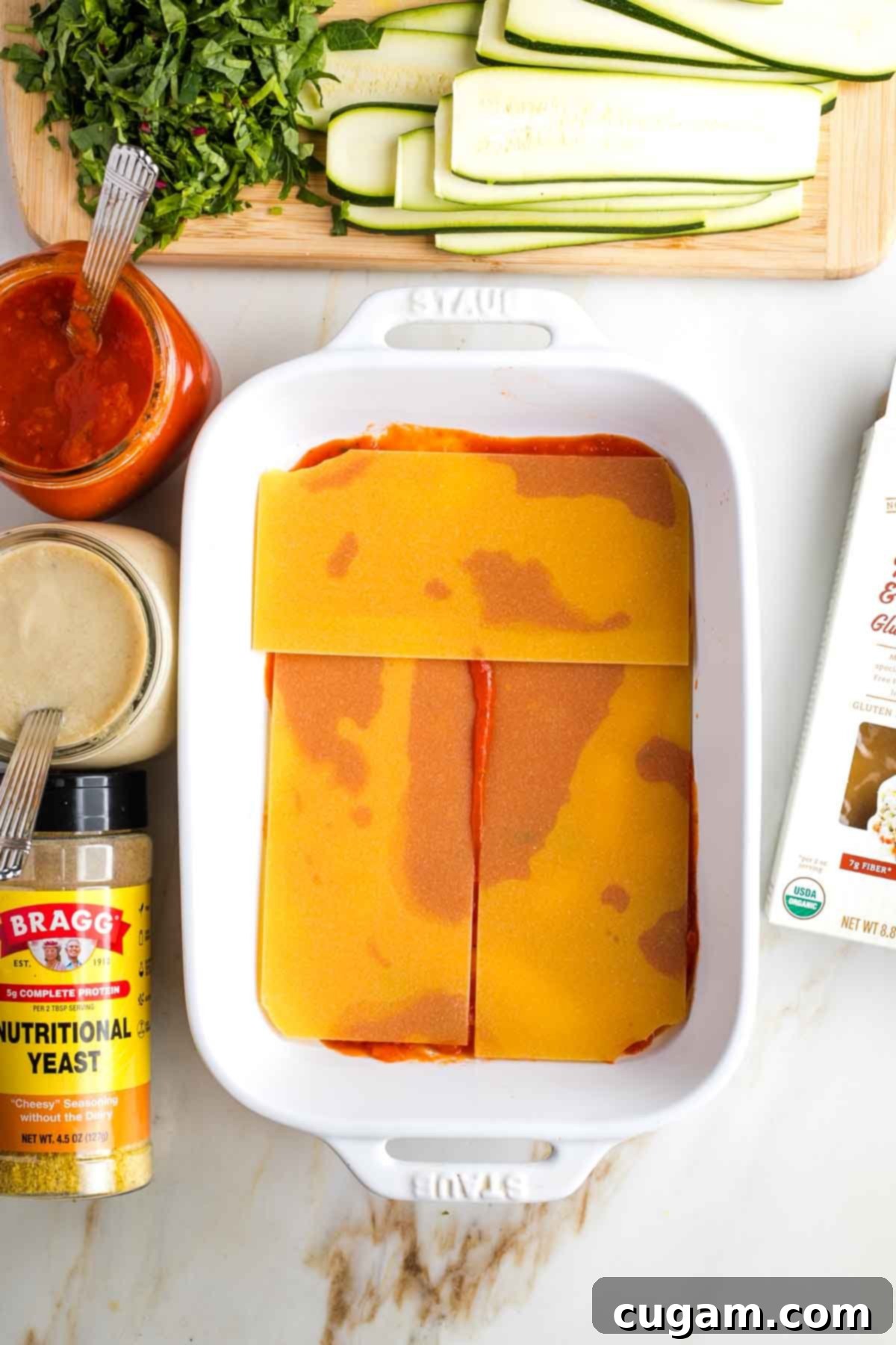 Baking dish with a layer of marinara sauce and a layer of uncooked lasagna noodles.