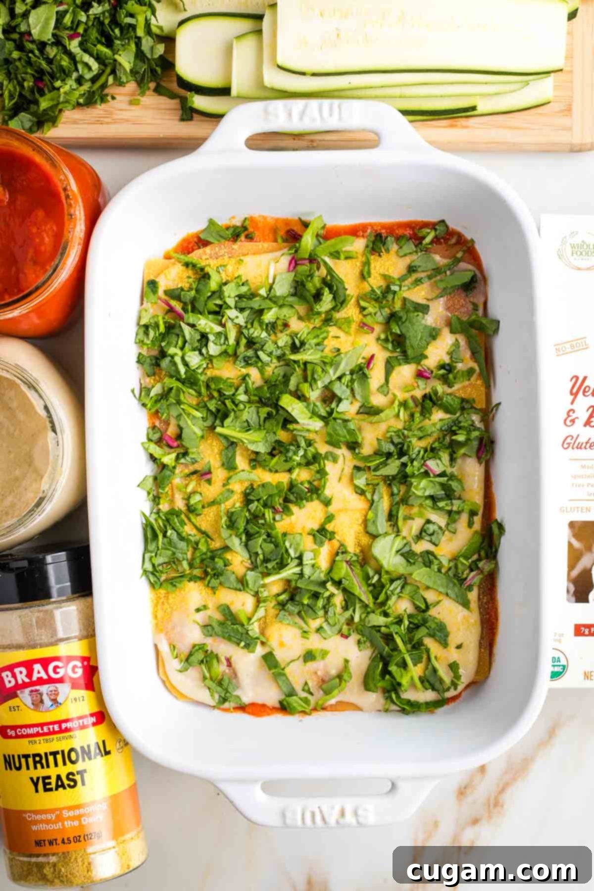 Layering a lasagna in a baking dish, chopped greens on top.