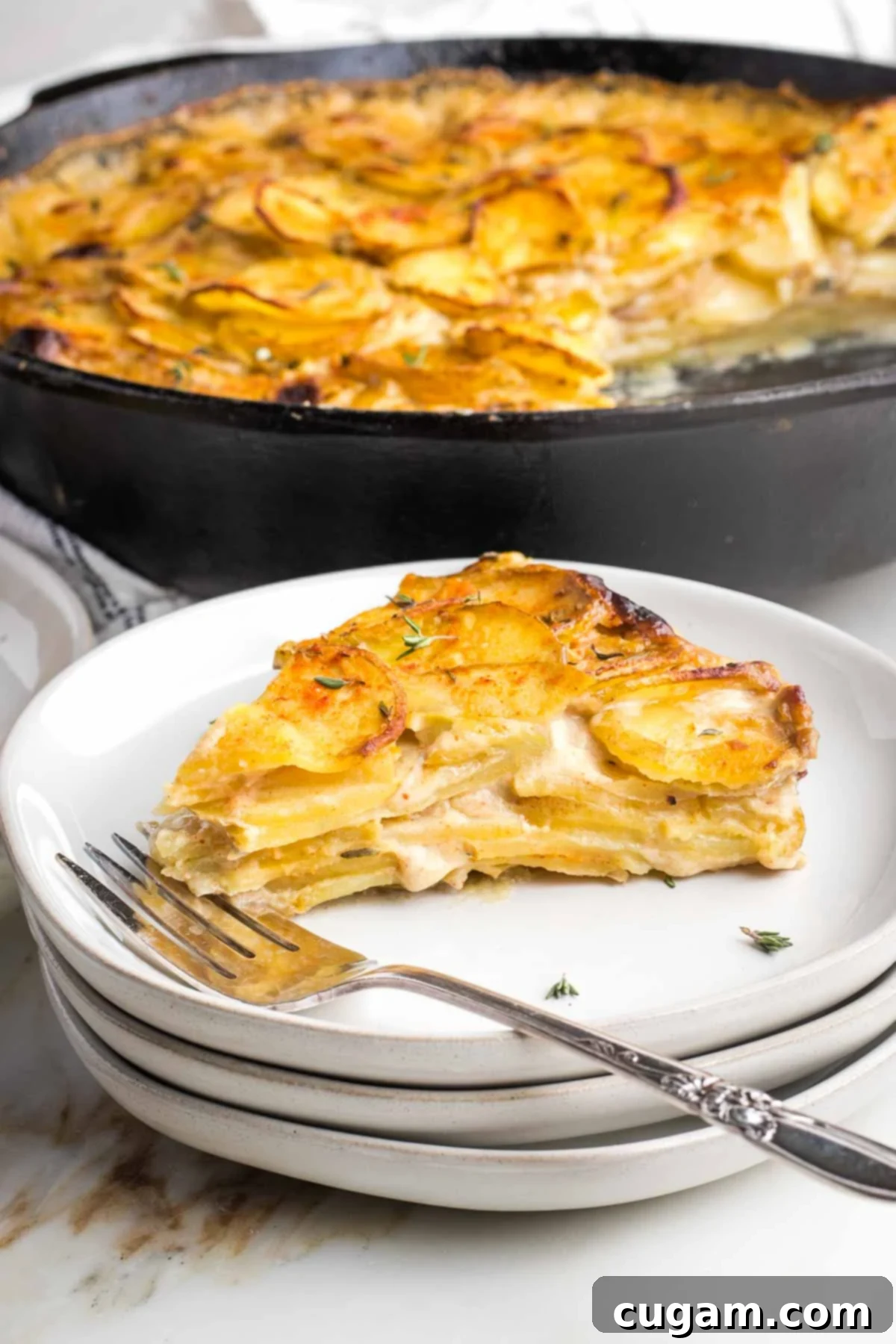 Slice of scalloped potatoes taken from a cast iron skillet, showcasing the creamy layers and crispy top.