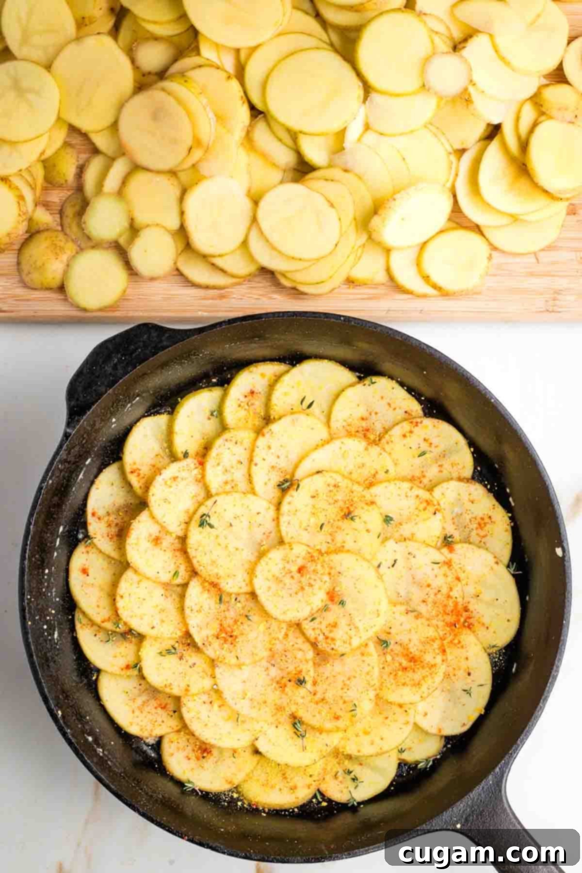 Thin slices of potatoes staggered to form a circular pattern in a cast iron skillet, sprinkled with paprika, salt, pepper and fresh thyme. 