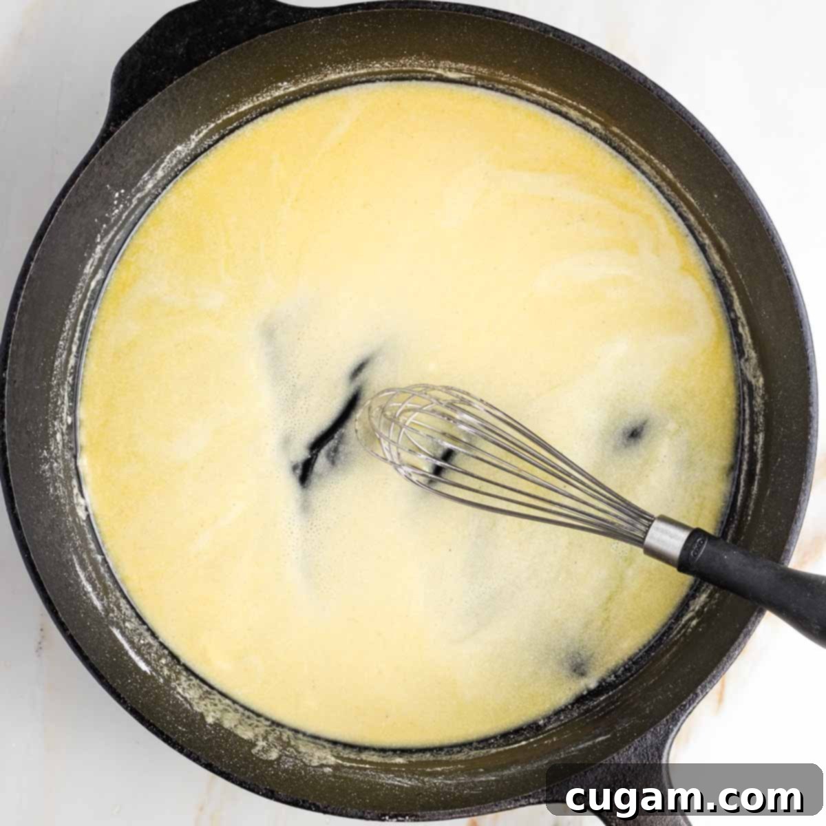 Whisking a classic white sauce together in a cast iron skillet.