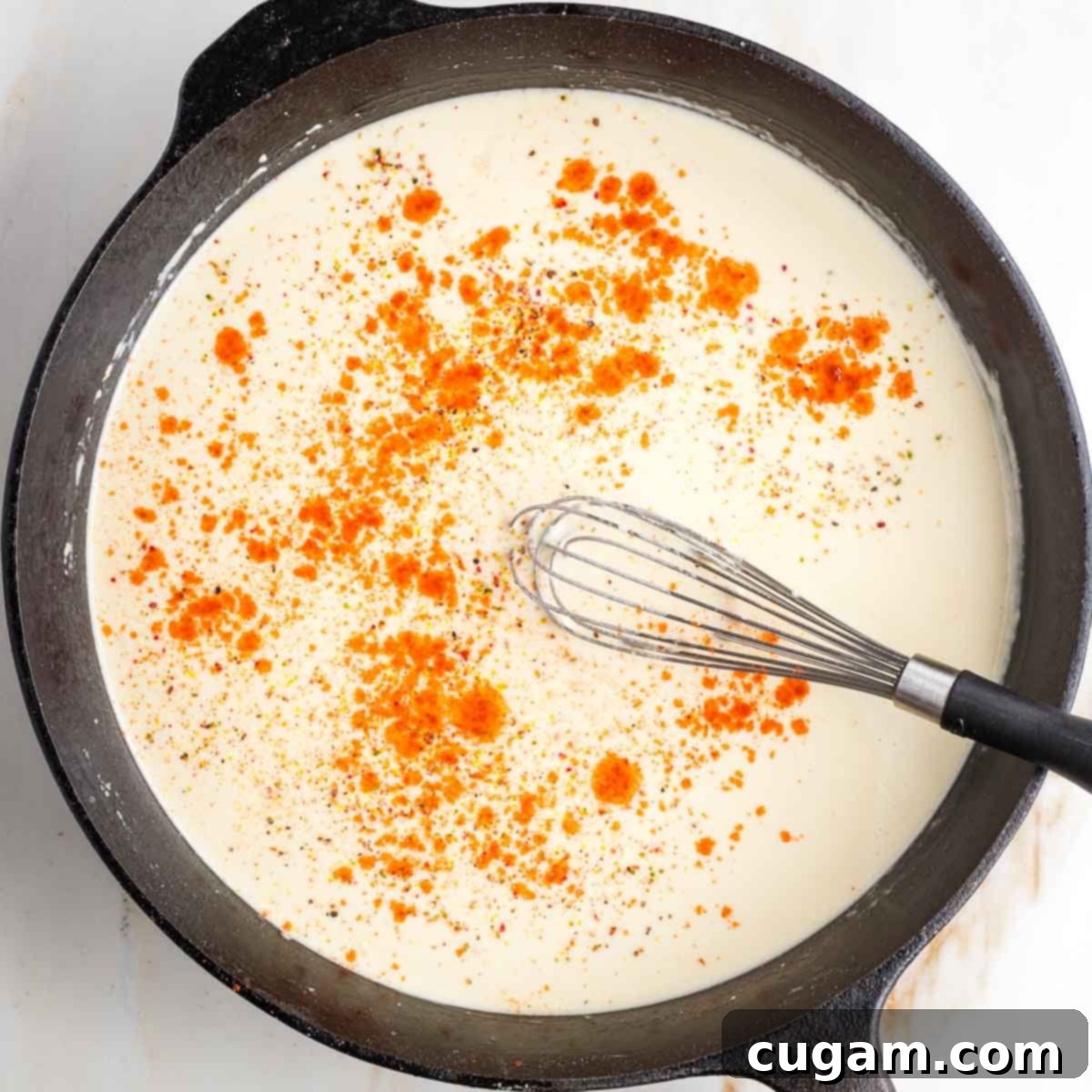 Whisking paprika, salt and pepper into a bechamel sauce in a cast iron skillet.