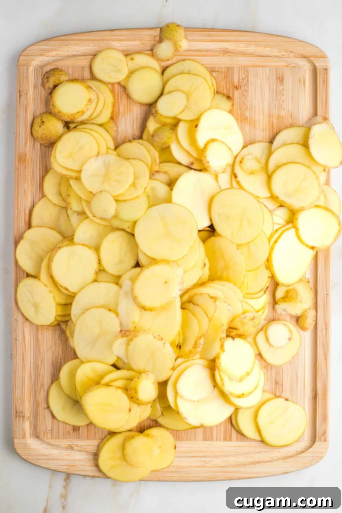 A pile of thinly sliced creamy yellow potatoes on a wooden board.