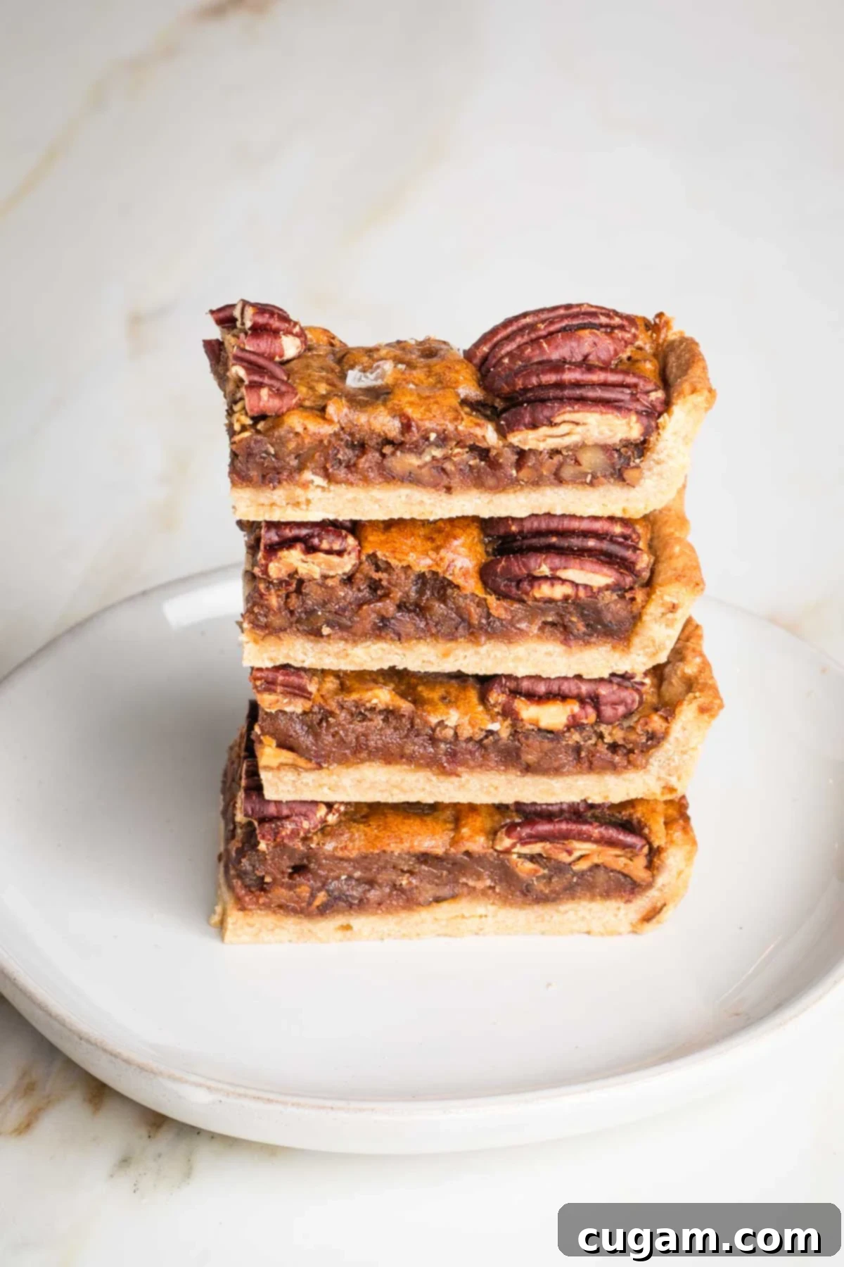 Side view of a stack of pecan pie bars, showing layers of crust, chewy filling and pecans on top. 