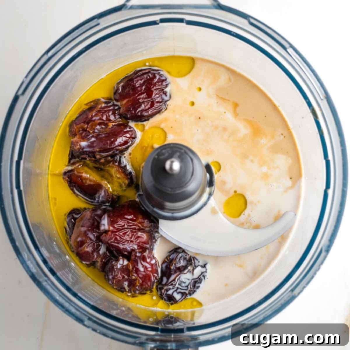 Food processor bowl with tahini, oil, dates and maple syrup distinctly visible. 