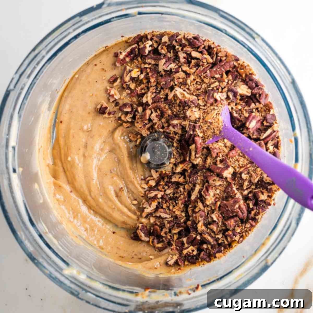 Chopped and toasted pecans on top of a caramel spread in the bowl of a food processor. 
