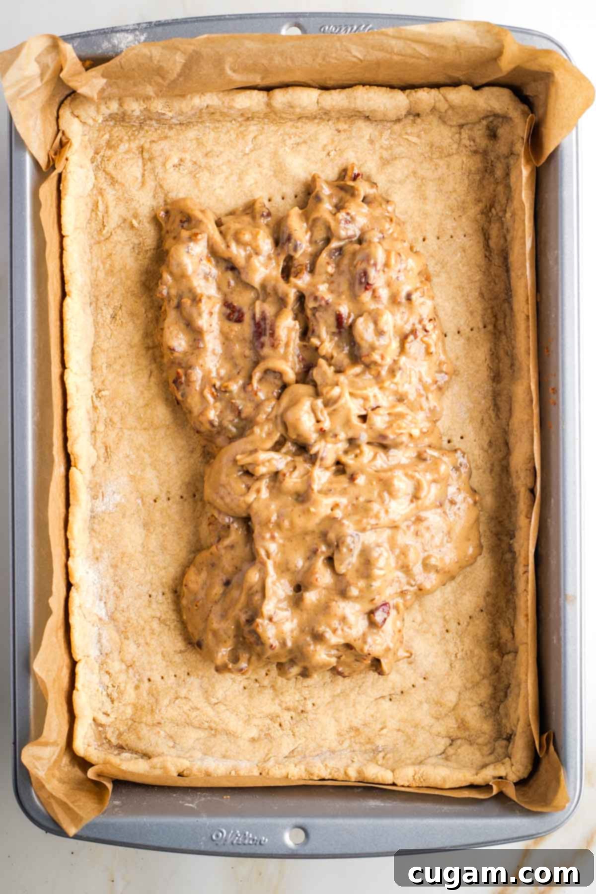 Caramel and pecan spread on top of a par baked rectangular pie crust in a baking pan. 